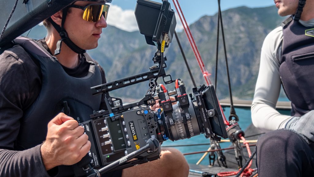 Camera operator shooting with an ARRI ALEXA 35 Xtreme rigged with a monitor, on a boat with mountains in the background