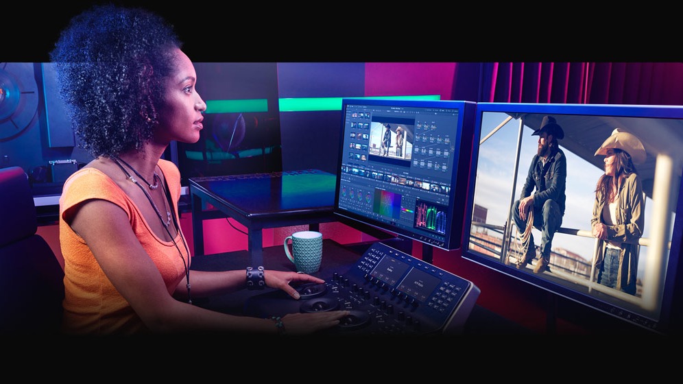 Colorist working at a DaVinci Resolve color grading panel with the interface visible on dual monitors