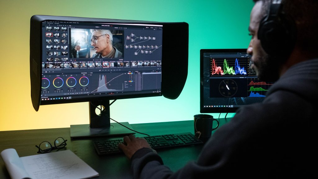 A colorist grading footage on dual monitors with color wheels and scopes visible