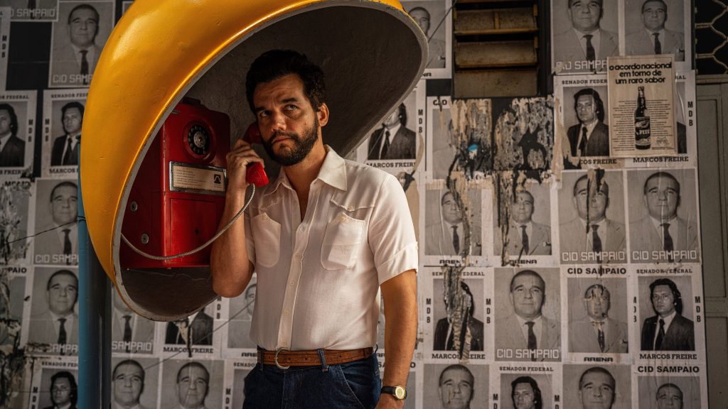 Wagner Moura as Marcelo in a yellow phone booth in The Secret Agent (2025), directed by Kleber Mendonca Filho, copyright Cinemascopio, MK Productions, Lemming Film, One Two Films, distributed by Neon