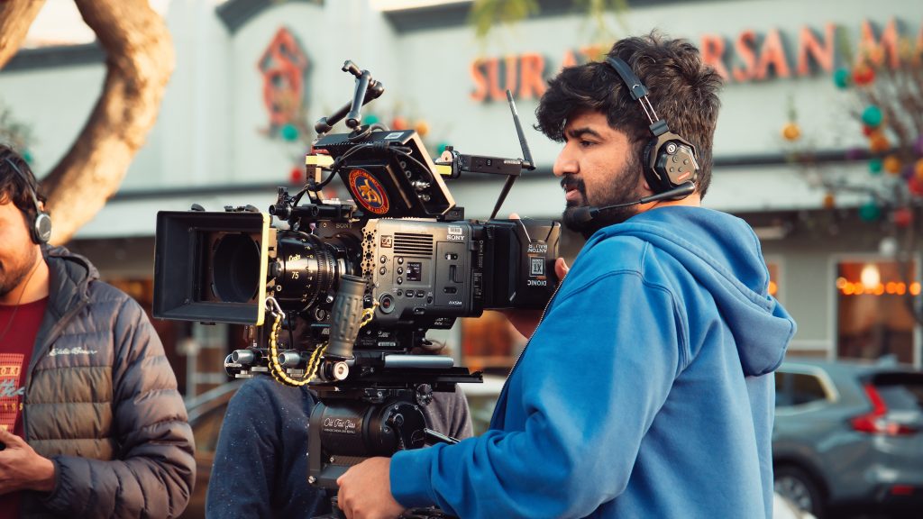 Cinematographer operating a Sony Venice cinema camera with vintage lenses on a film set, headphones on, crew visible in background