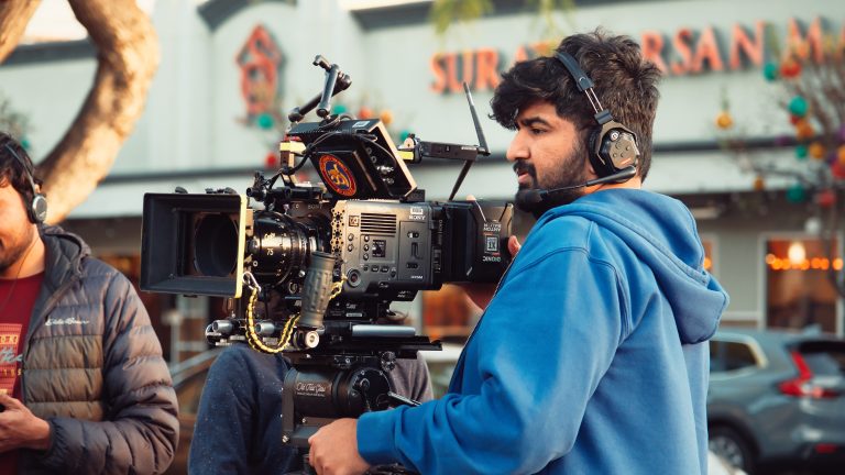 Cinematographer operating a Sony Venice cinema camera with vintage lenses on a film set, headphones on, crew visible in background