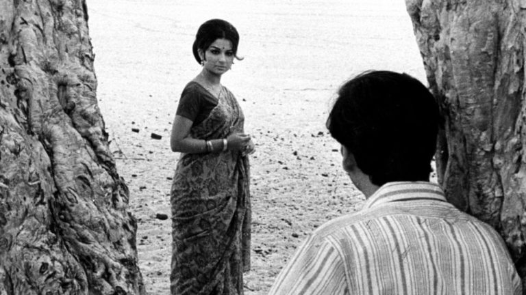 Black and white still from Satyajit Ray's Days and Nights in the Forest showing Aparna (Sharmila Tagore) standing between two trees while Asim looks on, 1970, Priya Films