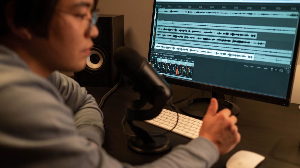 Audio editor with a studio microphone in front of a monitor showing stacked dialogue waveforms and a mixer in a DAW timeline